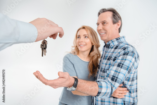 portrait of smiling couple receiving keys from new house on white