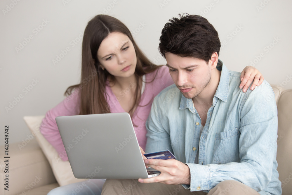 Young couple shopping online via laptop computer, e-commerce, banking support, financial services. Man holding plastic credit card, checking problems, security protection service, insufficient funds Young couple shopping online via laptop computer, e-commerce, banking support, financial services. Man holding plastic credit card, checking problems, security protection service, insufficient funds