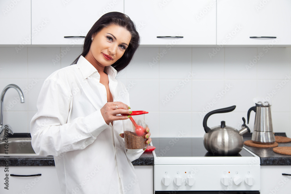 brunette woman with a spoonful of instant coffee in the kitchen brunette woman with a spoonful of instant coffee in the kitchen