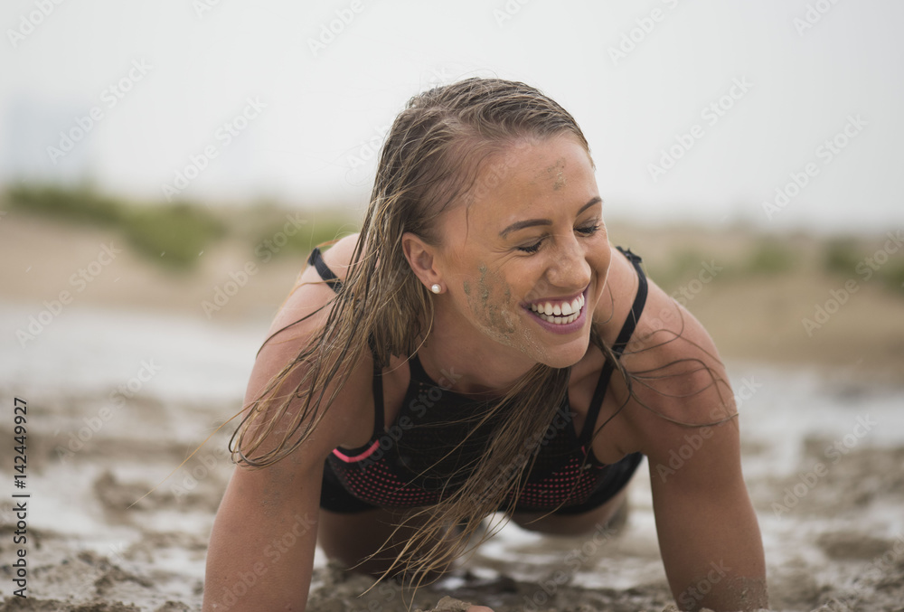 Strong athletic woman laughing with mud on her face crawling in mud or  extreme sport with clean background Photos | Adobe Stock