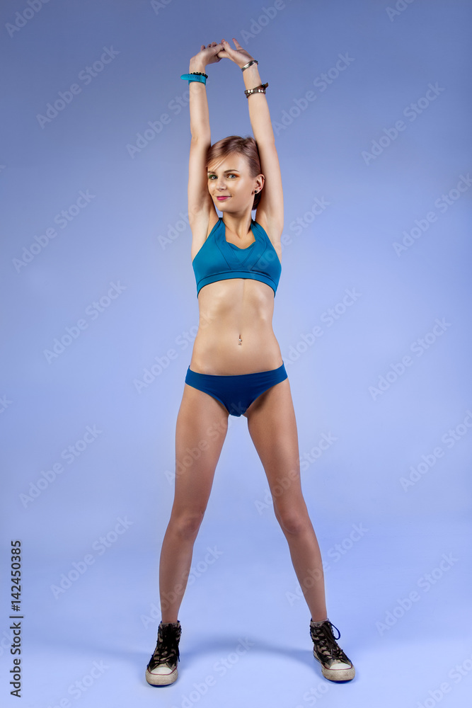 Young smiling woman in sports lingerie with raised arms on a blue