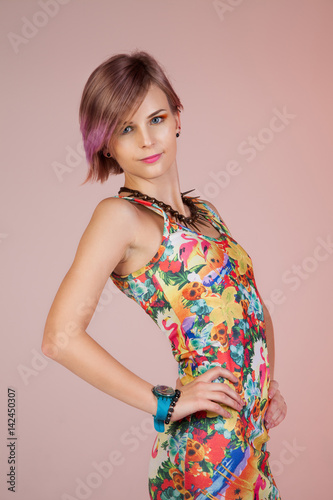 Young girl in a colorful dress with a partly colored hair, isolated on a pink background