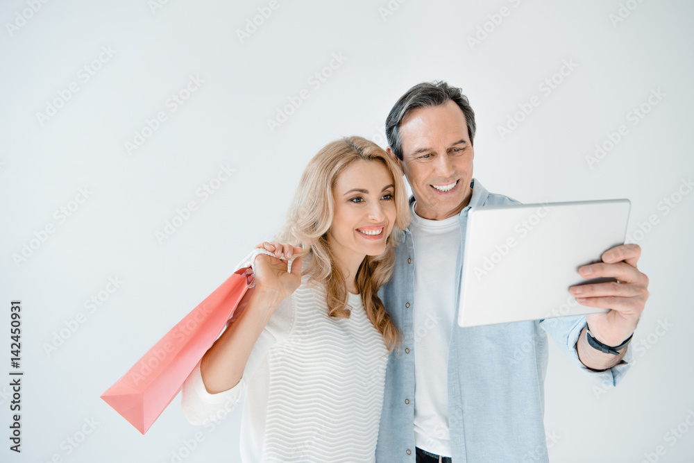 Happy couple with paper bag using digital tablet on grey Happy couple with paper bag using digital tablet on grey