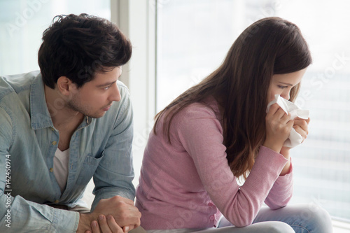 Sad upset girl crying, wiping tears with handkerchief, friend or boyfriend trying to comfort her at home, husband consoling depressed wife, support in difficult situation, compassion or apologize