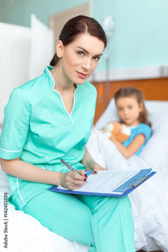 Woman doctor writing in clipboard diagnosis of sick little girl Woman doctor writing in clipboard diagnosis of sick little girl