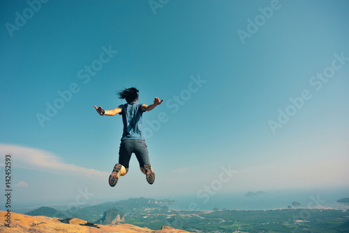 successful woman jumping on rocky mountain peak, freedom, risk, challenge, success concept