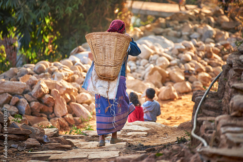 Nepalese woman carries huge wicker basket on her back at the street of Bandipur, Nepal photo