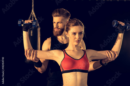 Bearded handsome man training young sporty woman with dumbbells