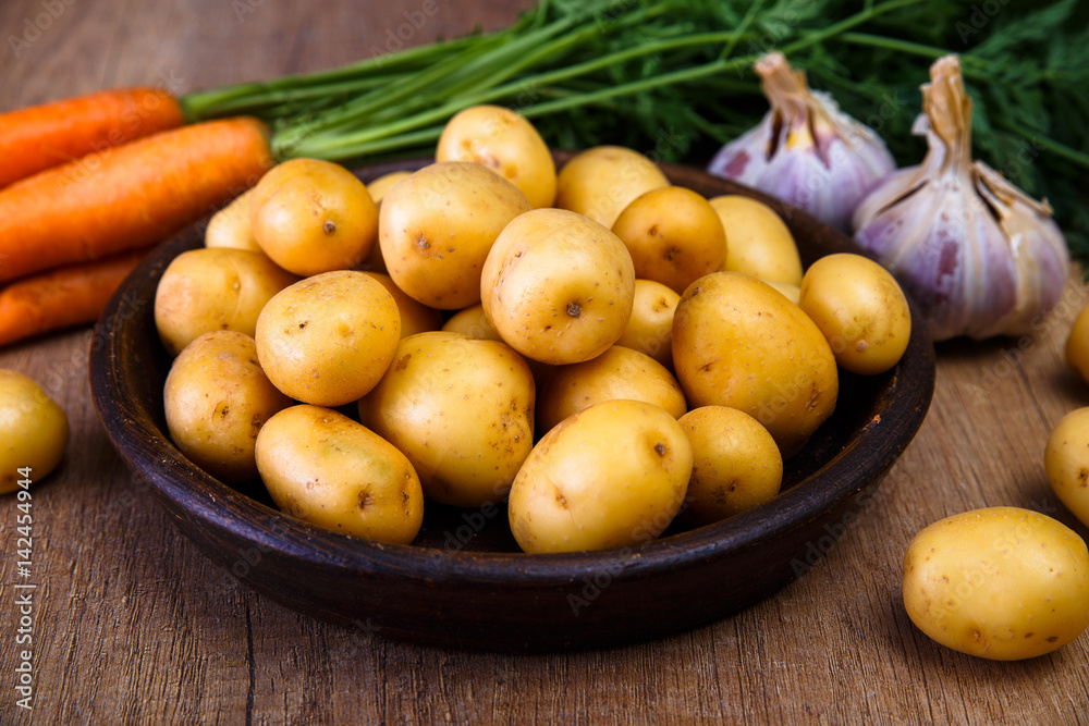 Potatoes in plate. Carrot, garlic and raw new potato. Fresh natural vegetables. Organic bio food on rustic wooden table. Potatoes in plate. Carrot, garlic and raw new potato. Fresh natural vegetables. Organic bio food on rustic wooden table.