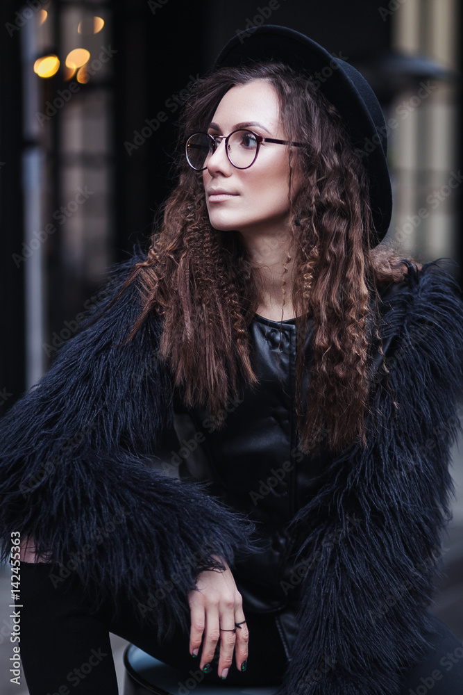 Portrait of a beautiful girl with brown eyes in glasses in a black hat and coat with fur in the cityscape looking away. The girl is like Harry Potter Portrait of a beautiful girl with brown eyes in glasses in a black hat and coat with fur in the cityscape looking away. The girl is like Harry Potter