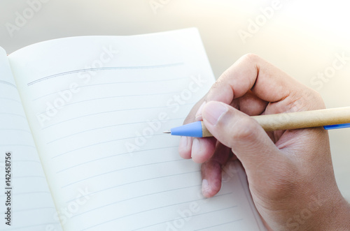 Hands with pen writing on notebook on nature light background