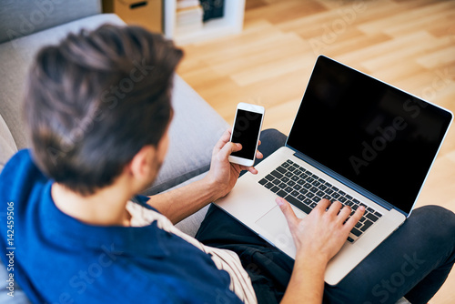 Laptop and smartphone mockup - man using his devices sitting on sofa