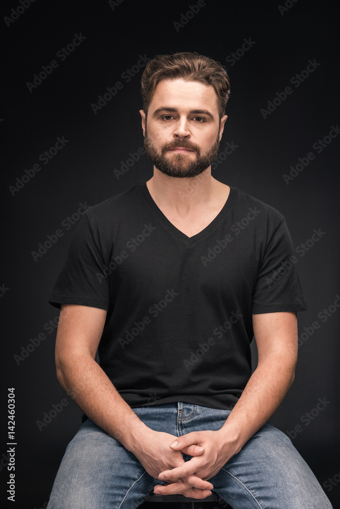 handsome bearded man sitting and looking at camera on black