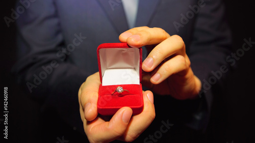 Man in a blue suit gives a ring with a diamond in a red box