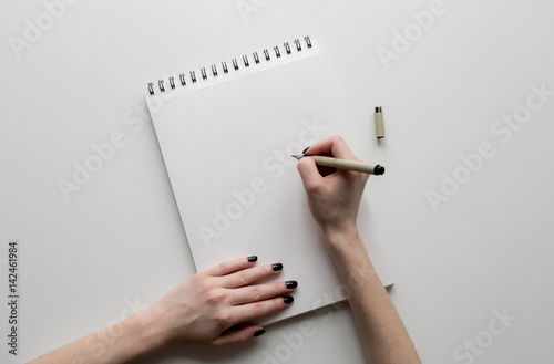 Woman hands holding paper sheet or notebook and pen. White table. Top view.