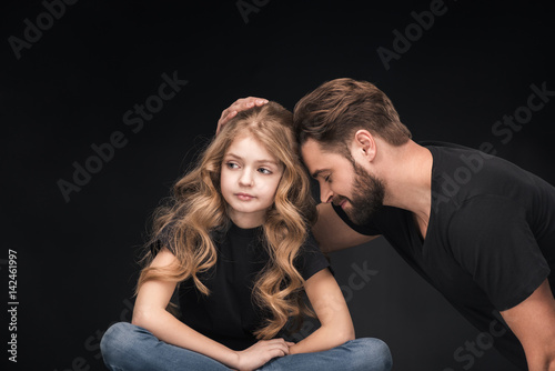 adorable little girl sitting and father hugging her on black