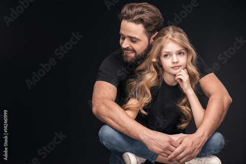 adorable little girl sitting and father hugging her on black