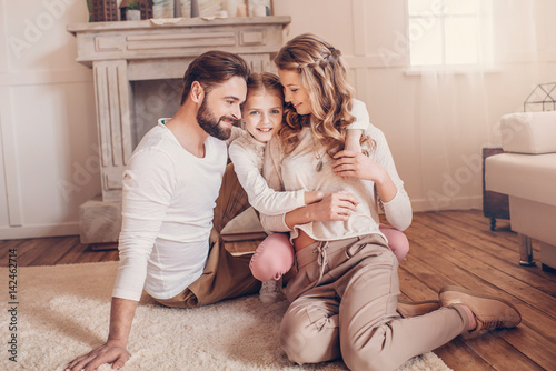 Happy young family with one child sitting on carpet and hugging at home
