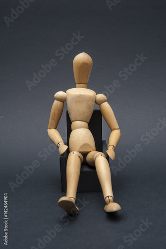 Person represented by a wooden dummy relaxing while sitting on an armchair in a comfortable position.