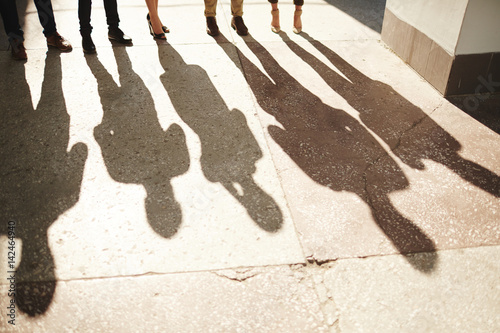 Shadows of five businesspeople standing outdoors, bright sunbeams illuminating shabby asphalt surface
