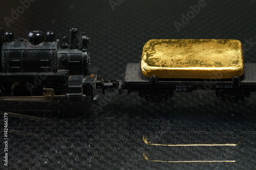 Gold bar put on the on the model railroad flatcar represent the business concept related idea.