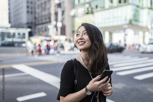 USA, New York City, Manhattan, young woman listening music with cell phone and earphones on the street photo