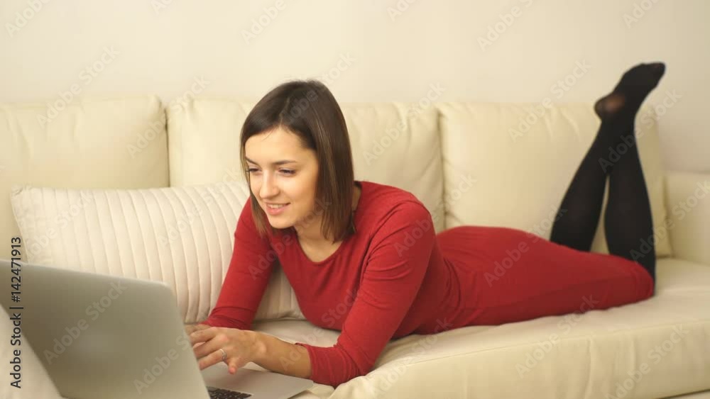 Attractive elegant woman lying down on hotel room sofa and working on laptop. Attractive elegant woman lying down on hotel room sofa and working on laptop.