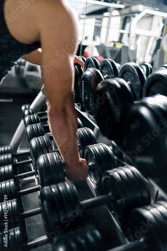 Closeup shot of muscular male arm picking up heavy dumbbells from equipment rack in modern gym