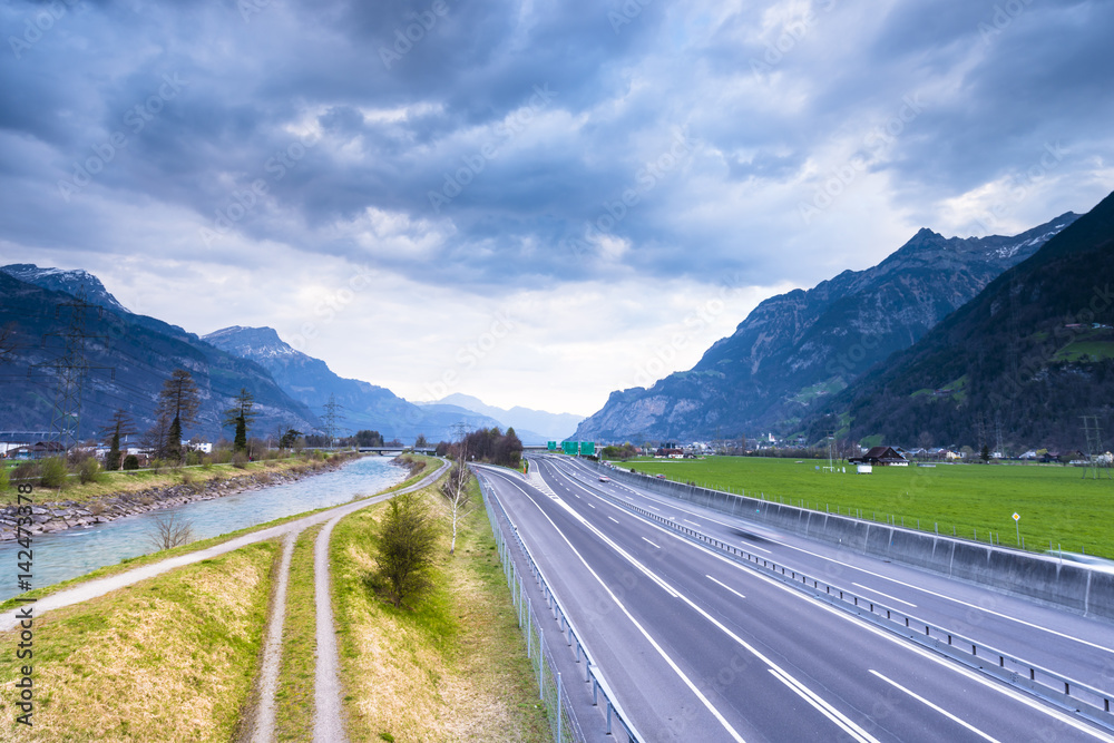 The roads lead to the distance. Several roads and a river. The sky in the clouds of the setting sun. Mountain landscape. Switzerland.