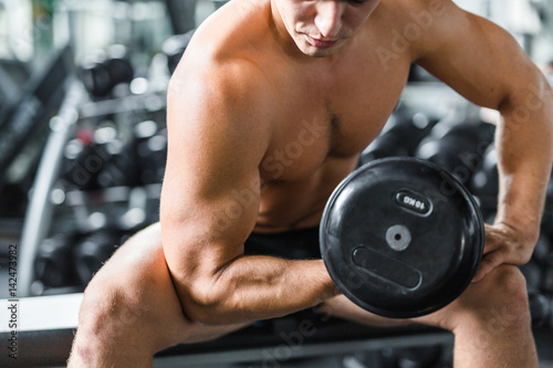 Fotografia Mid section portrait of shirtless muscular man doing arm exercise working out wi