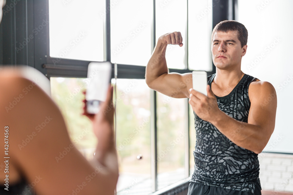 Portrait of proud bodybuilder boasting his arm muscles taking selfie in