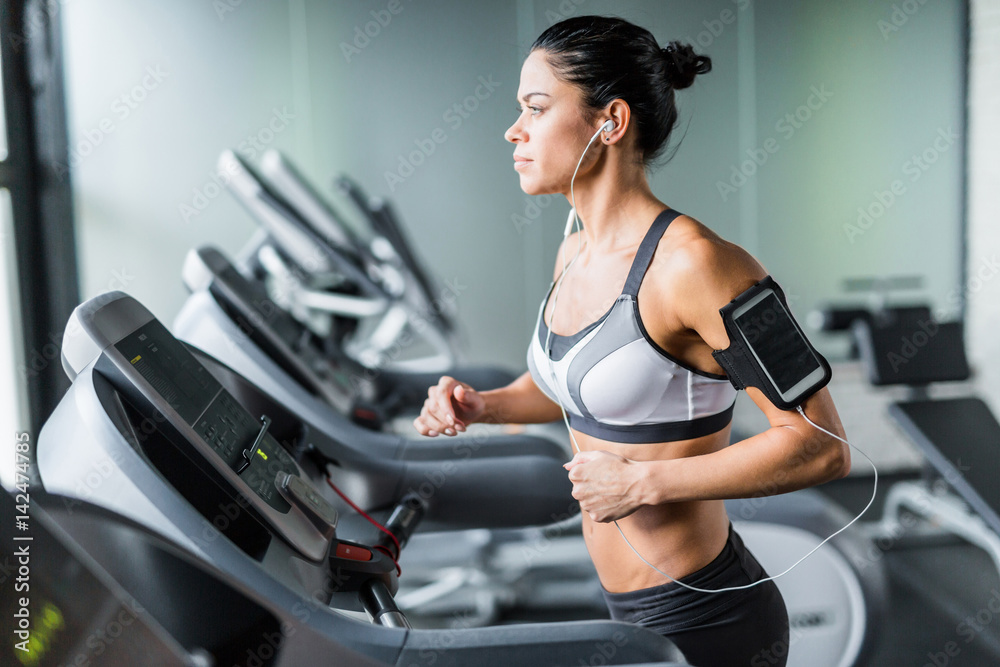 Portrait of sportive brunette woman exercising on treadmill in gym listening to music using shoulder smartphone holder Portrait of sportive brunette woman exercising on treadmill in gym listening to music using shoulder smartphone holder