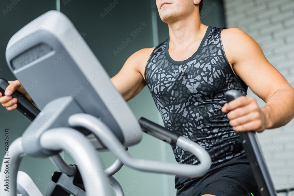 Closeup portrait of muscular sportive man running using elliptical trainer during workout in modern gym Closeup portrait of muscular sportive man running using elliptical trainer during workout in modern gym