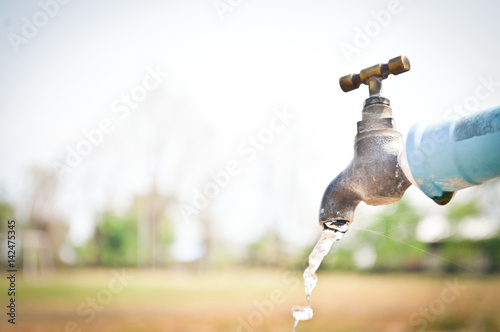 Water drop from water tap.Wasting water.Brass water tap in nature background.