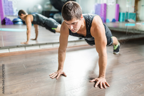 Portrait of strong muscular man doing push ups during workout in modern fitness studio next to mirror