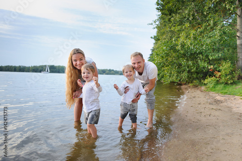 Happy family - father, mother, two sons on the beach with their feet in the water at sunset