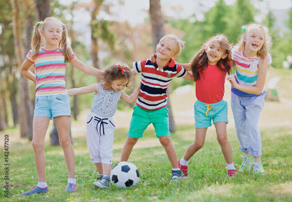 Little kids in summer wear standing in front of ball in park, embracing each other and smiling cheerfully Little kids in summer wear standing in front of ball in park, embracing each other and smiling cheerfully