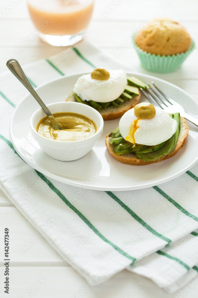 Vegetarian breakfast: avocado toast with poached eggs and mustard, orange juice,muffin on white wooden background. Selective focus Vegetarian breakfast: avocado toast with poached eggs and mustard, orange juice,muffin on white wooden background. Selective focus