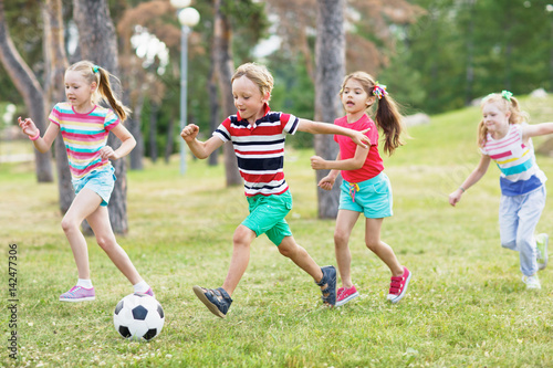 Elementary school kids in summer wear playing soccer on green lawn in park