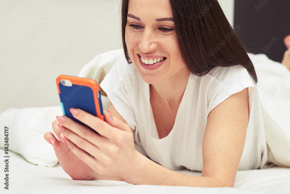 Smiley brunette lying on the bed with a telephone