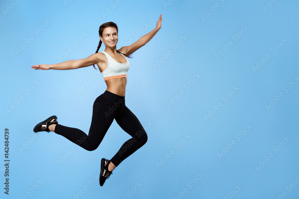 Nice girl in cool sportswear jumping high with hands up