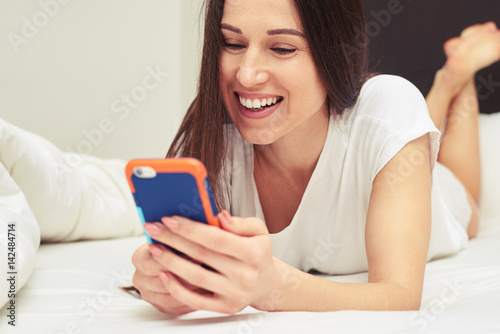 Delighted female typing on the cellphone while lying on the bed