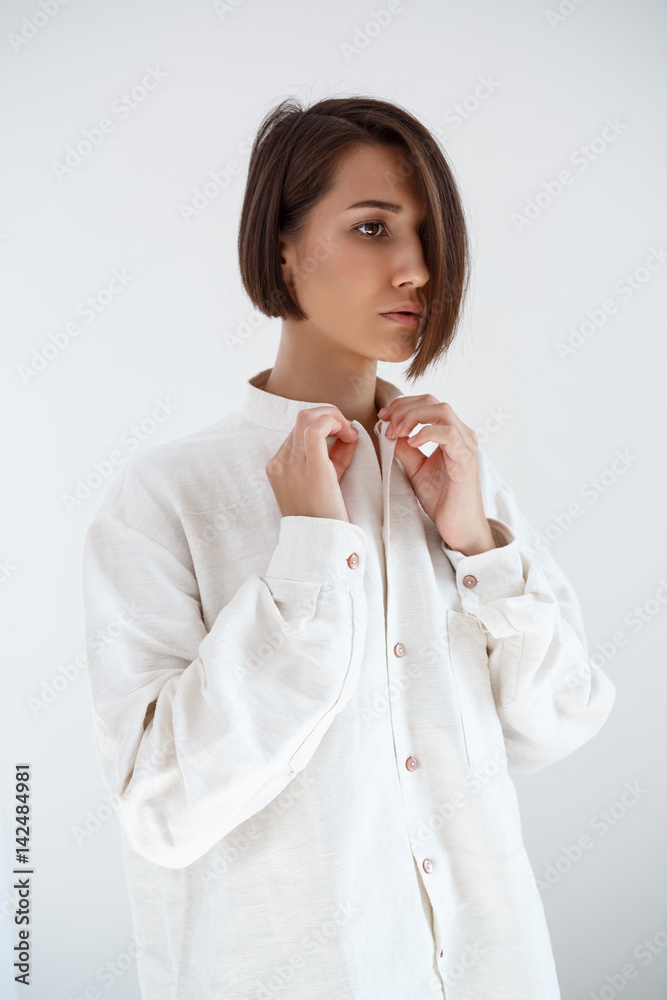 Young beautiful brunette girl fastening shirt over white background. Young beautiful brunette girl fastening shirt over white background.