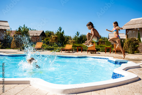 Cheerful children rejoicing, jumping, swimming in pool.