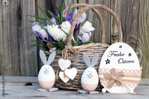 Text Frohe Ostern mit Osterhasen Ei und Weidenkorb mit Krokusse rustikal vor Holzhintergrund