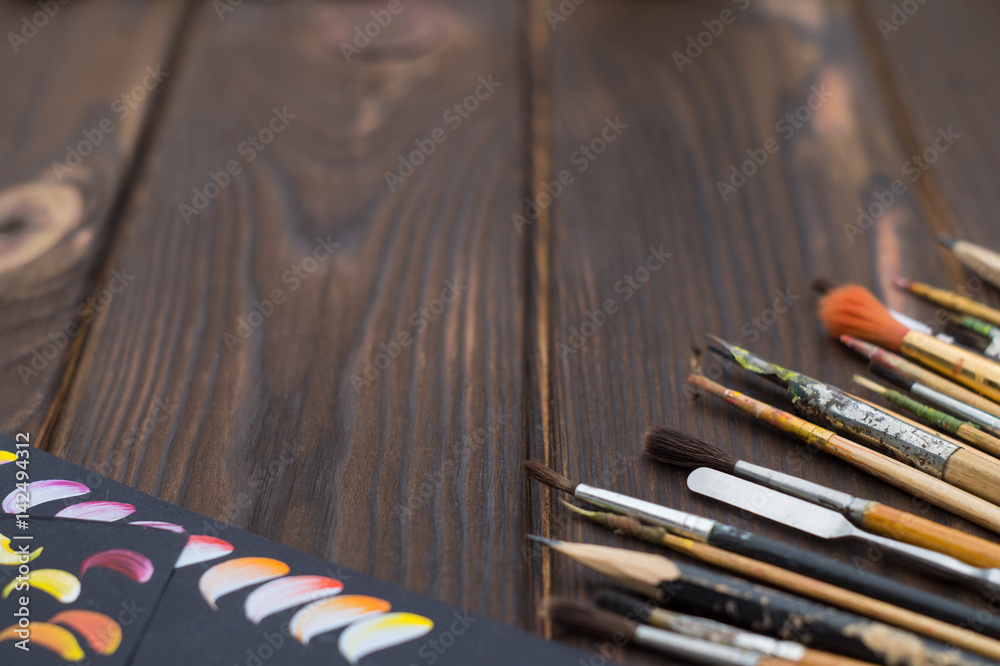 Fototapeta premium Brushes and sketches are spread out on a dark wooden surface