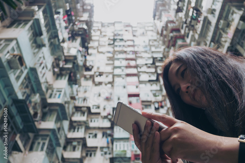 Low angle image of a woman using mobile phone with a crowded residential building in community in Quarry Bay, Hong Kong background  © Farknot Architect