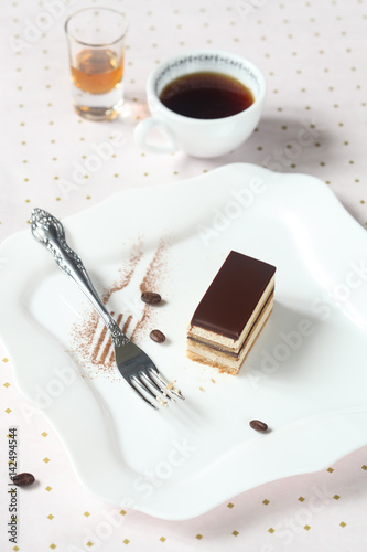 Tableau sur toile Piece of Opera Chocolate Coffee Cake on square white plate and cup of coffee, on light background