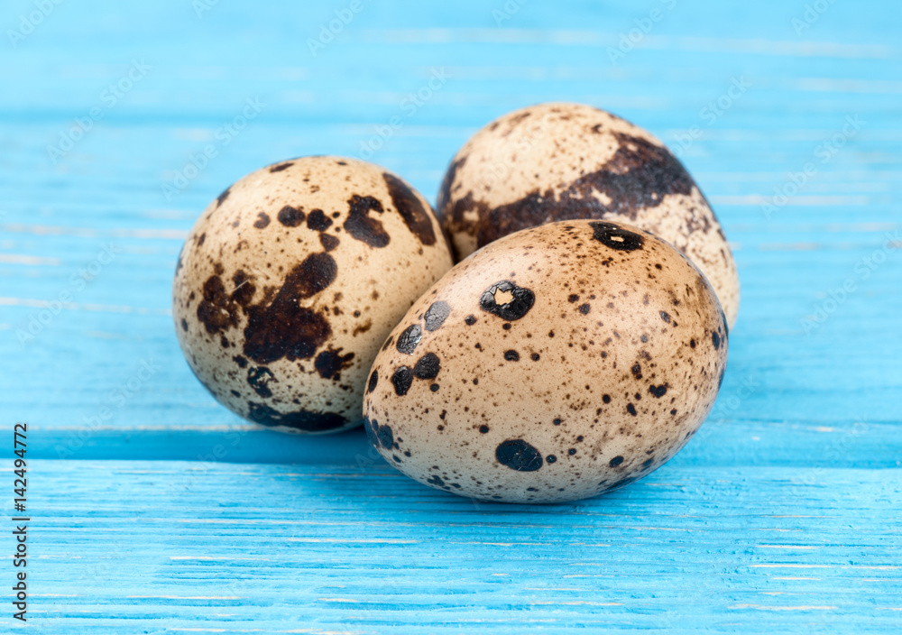 Obraz premium Three fresh quail eggs on a blue table, close-up