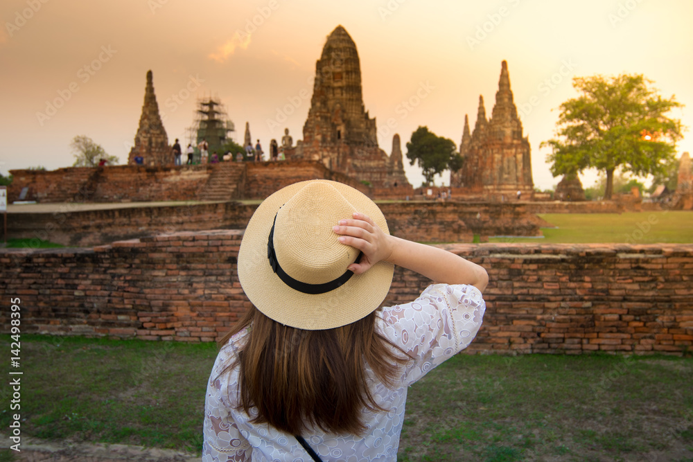 Lady tourist is touching her hat and looking at Wat Chaiwatthanaram while sunset in Ayutthaya ancient city.